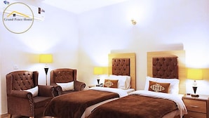 Una habitación de hotel con dos camas, un sillón marrón y una mesita de noche con lámpara.