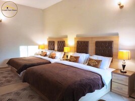 Habitación de hotel con dos camas, una mesita de noche con lámpara y una lámpara de pared.
