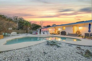 A backyard with a swimming pool, outdoor furniture, and a building with a lighted exterior.