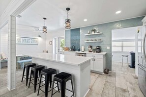A modern kitchen with a central island, bar stools, and a 'NO WAKE ZONE' sign.