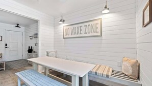 A room with a white wall, a 'NO WAKE ZONE' sign, a white table, a blue bench, and a bench with pillows. - Somewhere To Beach - Jacksonville Beach, Florida (Jacksonville Beach)