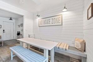 A room with a white wall, a 'NO WAKE ZONE' sign, a white table, a blue bench, and a bench with pillows.