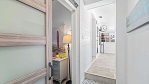 A hallway with a wooden door, a desk with a lamp, and a view into a room with a tiled floor. - Somewhere To Beach - Jacksonville Beach, Florida (Jacksonville Beach)