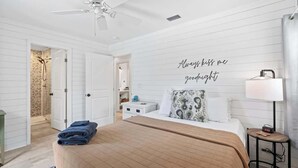 A bedroom with a bed, a bedside table, a lamp, a ceiling fan, and a wall with a quote. - Somewhere To Beach - Jacksonville Beach, Florida (Jacksonville Beach)