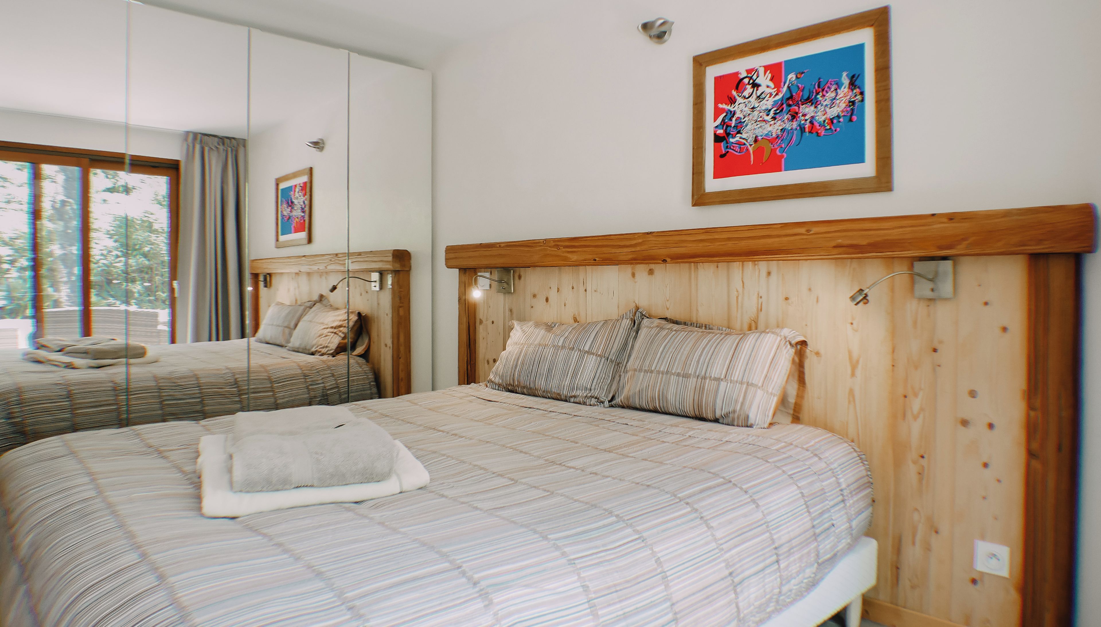 A hotel room with two beds, wooden headboards, a large window, and a framed abstract painting.