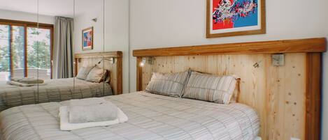 A hotel room with two beds, wooden headboards, a large window, and a framed abstract painting.