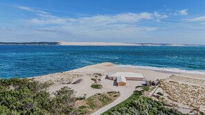 A coastal property with a sandy beach, a small building with a white roof, and a clear view of the ocean. - Villa à la Pointe du Cap Ferret (Lège-Cap-Ferret)