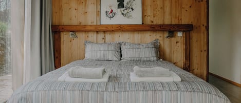 A bedroom with a wooden headboard, a bed with striped bedding, two pillows, and two towels.
