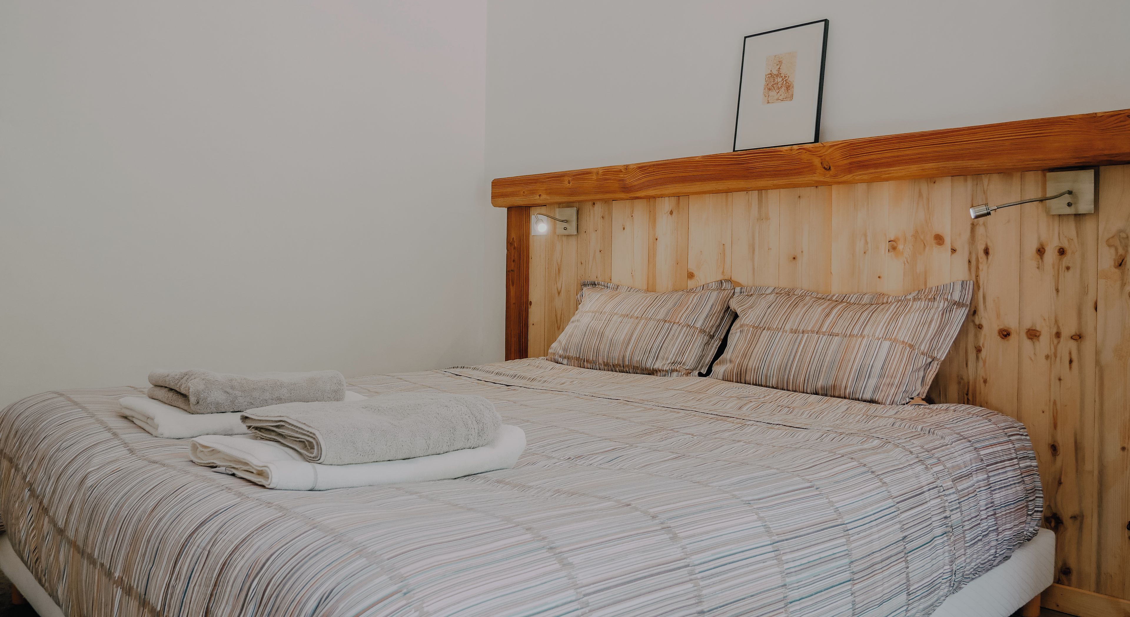 A bed with a wooden headboard, two pillows, and folded towels.