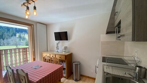 Uma cozinha compacta com mesa e cadeiras de madeira, pia embutida e televisão fixada na parede.