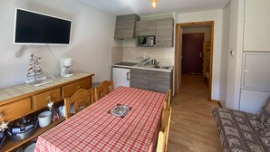 Quarto compacto com cozinha compacta, área de refeições com mesa xadrez vermelha, televisão e uma pequena árvore de Natal.