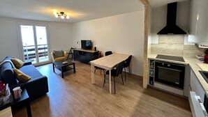 A compact living space with a sofa, a dining table, a TV, and a kitchenette.