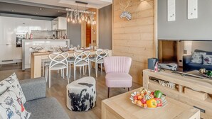 Una sala de estar moderna con un sofá gris, una mesa de centro de madera con fruta, un sillón rosa y un mueble para televisor.