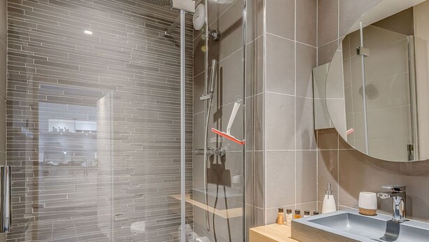 Un bany modern amb dutxa d'ús de vidre, un tocador de fusta amb un lavabo i un mirall gran.