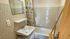 A bathroom with a sink, toilet, and bathtub. There is a mirror above the sink and a shower curtain with cartoon characters. The walls have a patterned tile design. - Functional apartment in Châtel center, near ski lifts (Châtel)