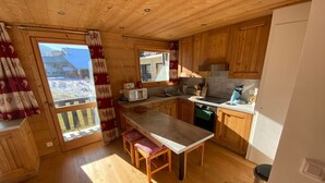 A cozy kitchen with wooden cabinets, a central island, and a view to the outside. - Functional apartment in Châtel center, near ski lifts (Châtel)