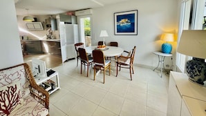 A modern kitchen with white cabinets, a dining area with a round table and chairs, and a large window with a view of greenery.
