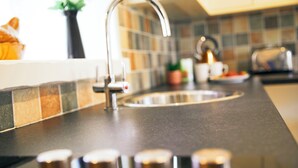 Une cuisine au design moderne, dotée d’un évier en acier inoxydable, d’une hotte aspirante et d’un dosseret carrelé.