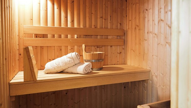 Un sauna en bois avec un banc, une serviette et un seau en bois.