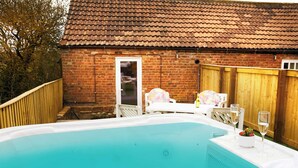 Un jacuzzi dans un jardin, avec une maison en briques et une clôture en bois.