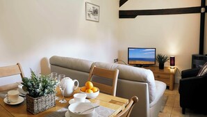 Un salon confortable avec un canapé, une table à manger sur laquelle se trouve un saladier rempli de fruits, une plante et un téléviseur.