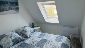 Ein Schlafzimmer mit einem Bett, einem Nachttisch, einer Lampe, einem Fenster und einem Gemälde an der Wand.
