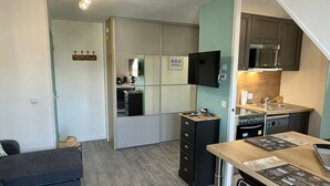 Eine kompakte Küche mit Mikrowelle, Herd und Spüle. Ein Esstisch mit Speisekarte und eine kleine Couch sind vorhanden.