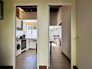 A kitchen with a washing machine, a coffee maker, and a dining area with chairs and a table.