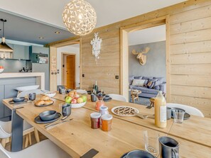 A modern kitchen with wooden accents, a dining area with a wooden table set for a meal, and a cozy living space with a sofa and decorative wall art. - Premium Apartment 4* - 5 rooms - 8 guests (Tignes)