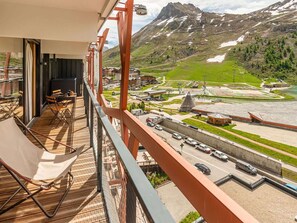 A balcony with a view of a mountainous landscape, a parking area, and a building with a unique roof structure. - Premium Apartment 4* - 5 rooms - 8 guests (Tignes)