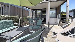 Een overdekt terras met een tafel en stoelen, een groene parasol en uitzicht op het aangrenzende gebouw.