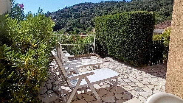 Un patio al aire libre con suelo de piedra y sillas de metal blanco.