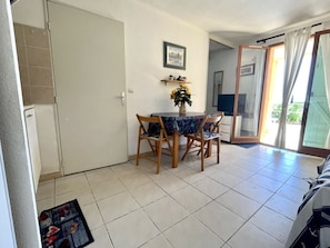 Un área de comedor con una mesa y sillas, un estante pequeño con objetos decorativos y una puerta que da a otra habitación.
