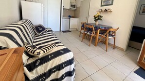 Un espacio habitable compacto con un sofá a rayas, una mesa de comedor con sillas, una pequeña kitchenette y un microondas.