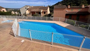 Una piscina con valla blanca, rodeada de pavimento de baldosas y vistas a casas al fondo.