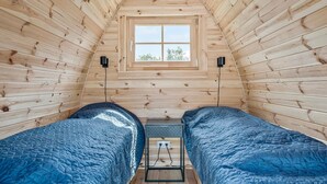 Acogedora habitación tipo cabaña con dos camas, una ventana y una mesita con toma de corriente.