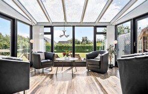 Un salón del vidrio con techo de cristal, dos sofás de cuero, una mesa redonda con flores y vista a un jardín.