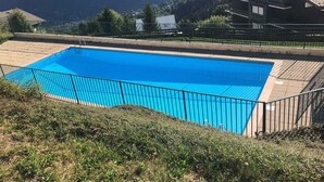 A rectangular swimming pool with a black metal fence, surrounded by a grassy area and a mountainous backdrop. - 2-room apartment calm near slopes, 6 people (Saint-Gervais-les-Bains)