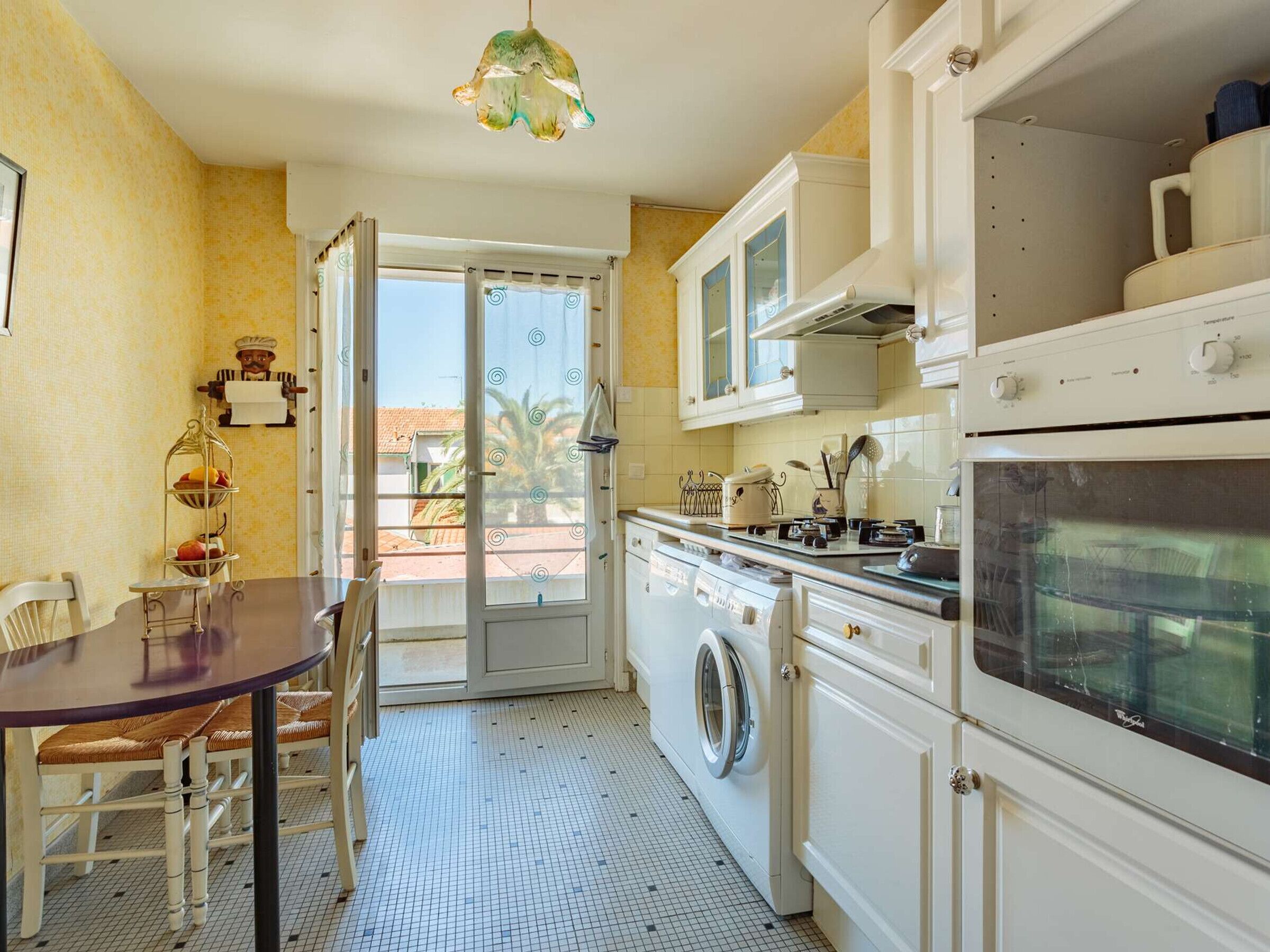 Una cucina compatta con lavatrice, un tavolo da pranzo con sedie e vista sull'esterno da una porta aperta.