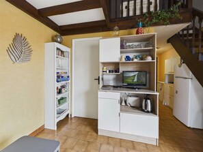 Cocina compacta con televisor integrado, muebles blancos y una escalera que sube a un nivel superior.