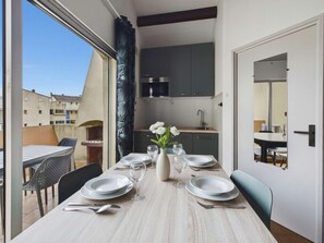 Un comedor con una mesa dispuesta para cuatro personas, un jarrón con flores y vistas al exterior.