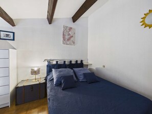 Un dormitorio con cama, mesita de noche, lámpara, maleta, cómoda y un sol decorativo en la pared.