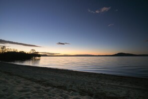 A beach with calm water and a clear sky. - Cooper's Lakeside - Lakefront, Kayaks, Sleeps 5 (Rotorua)