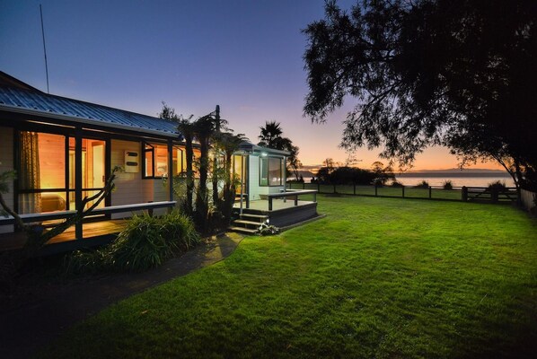 A modern house with a covered porch, a glass conservatory, and a well-maintained lawn. - Cooper's Lakeside - Lakefront, Kayaks, Sleeps 5 (Rotorua)