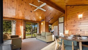 Interior acogedor de una cabaña con techo de madera, un sofá, una mesa de comedor con sillas y una chimenea.