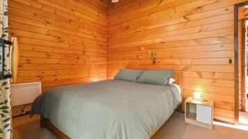 A wooden-paneled room with a bed, a bedside table with a lamp, and a radiator.