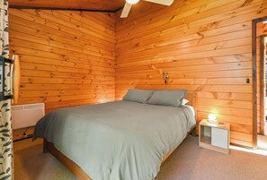 A wooden-paneled room with a bed, a bedside table with a lamp, and a radiator. - Cooper's Lakeside - Lakefront, Kayaks, Sleeps 5 (Rotorua)