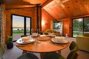 A wooden interior with a dining table set for four, a sofa, and a view of the outdoors. - Cooper's Lakeside - Lakefront, Kayaks, Sleeps 5 (Rotorua)