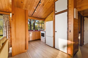 A compact kitchen with wooden cabinets, a refrigerator, and a stove. - Cooper's Lakeside - Lakefront, Kayaks, Sleeps 5 (Rotorua)