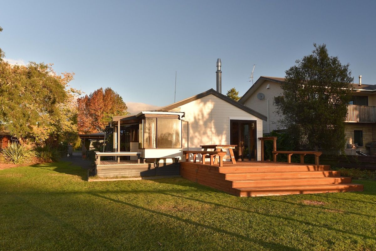 A residential property with a covered patio area, a wooden deck, and a small building with a chimney.